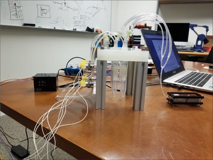 The experimental setup. The sensor sits atop the small glass box (left). A small amount of liquid containing VOCs (right) is added to the box, where it is drawn into the sensor via sniffing.