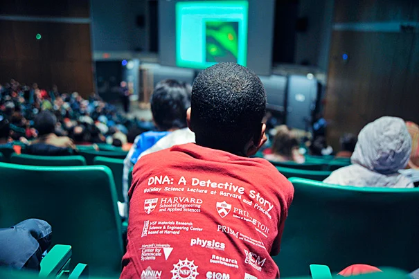 2014 Holiday Lecture with student in red shirt that displays all the sponsors